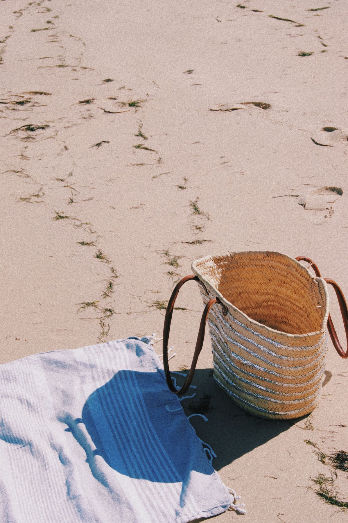 Woven beach bag and towel on white sand